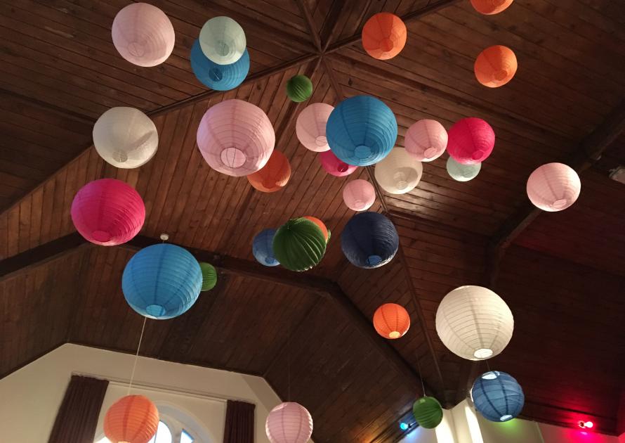 Coloured pom pom decorations suspended from Village Hall ceiling.