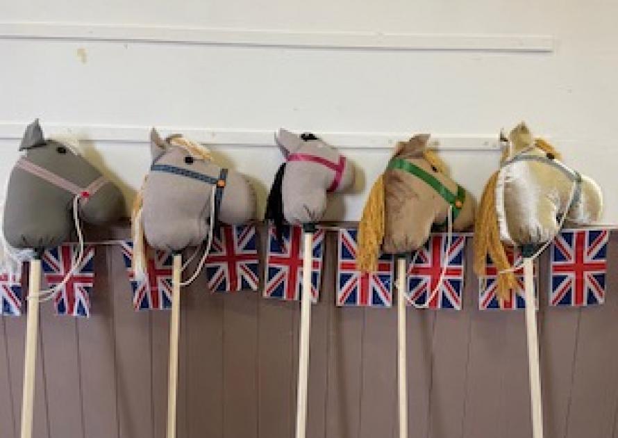 Row of 5 hobby horses leaning against a wall with Union Jack bunting