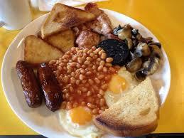 A full english breakfast t on a plate with sausage, bacon, egg, mushrooms and beans