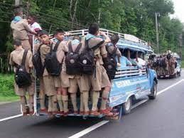 Picture of an overcrowded bus with passengers holding onto the outside