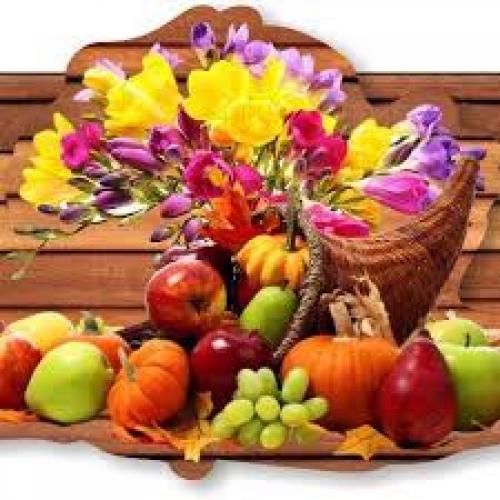 Picture of flower arrangement with selection of fruit in front of it.